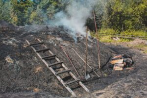 Rauchender Holzkohlemeiler mit Werkzeugen und Holz in einem Waldstück